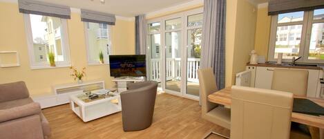 Una sala de estar moderna con un sofá, una mesa de centro y un televisor. Tiene un balcón con vistas al exterior.