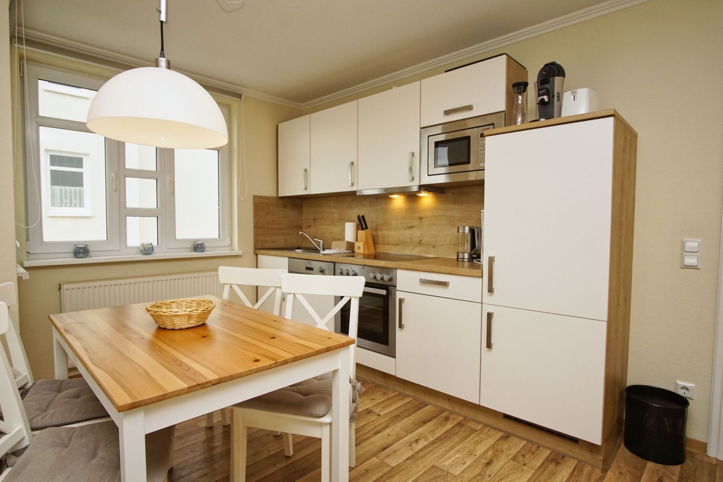 A compact kitchen with white cabinets, a wooden table, and a hanging light fixture.