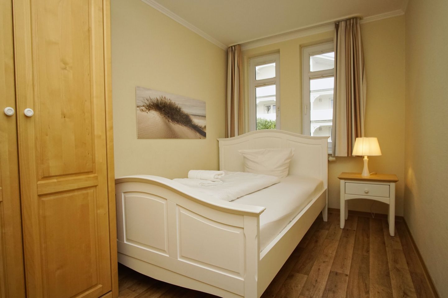 A bedroom with a bed, a bedside table with a lamp, a window with curtains, and a door.