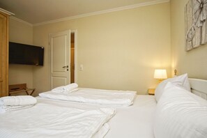 Una habitación de hotel con dos camas, un televisor, una silla de madera, una puerta y una lámpara fijada a la pared.