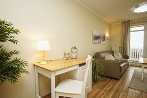 Una sala de estar acogedora con una mesa de madera, sillas blancas, un sofá marrón, una lámpara y una planta en maceta.