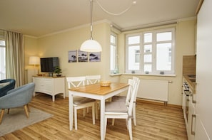 A modern kitchen with white cabinets, a wooden dining table, and a built-in oven. - With sea view and balcony, use of swimming pool and sauna - Sea view apartment 38 - (Göhren)