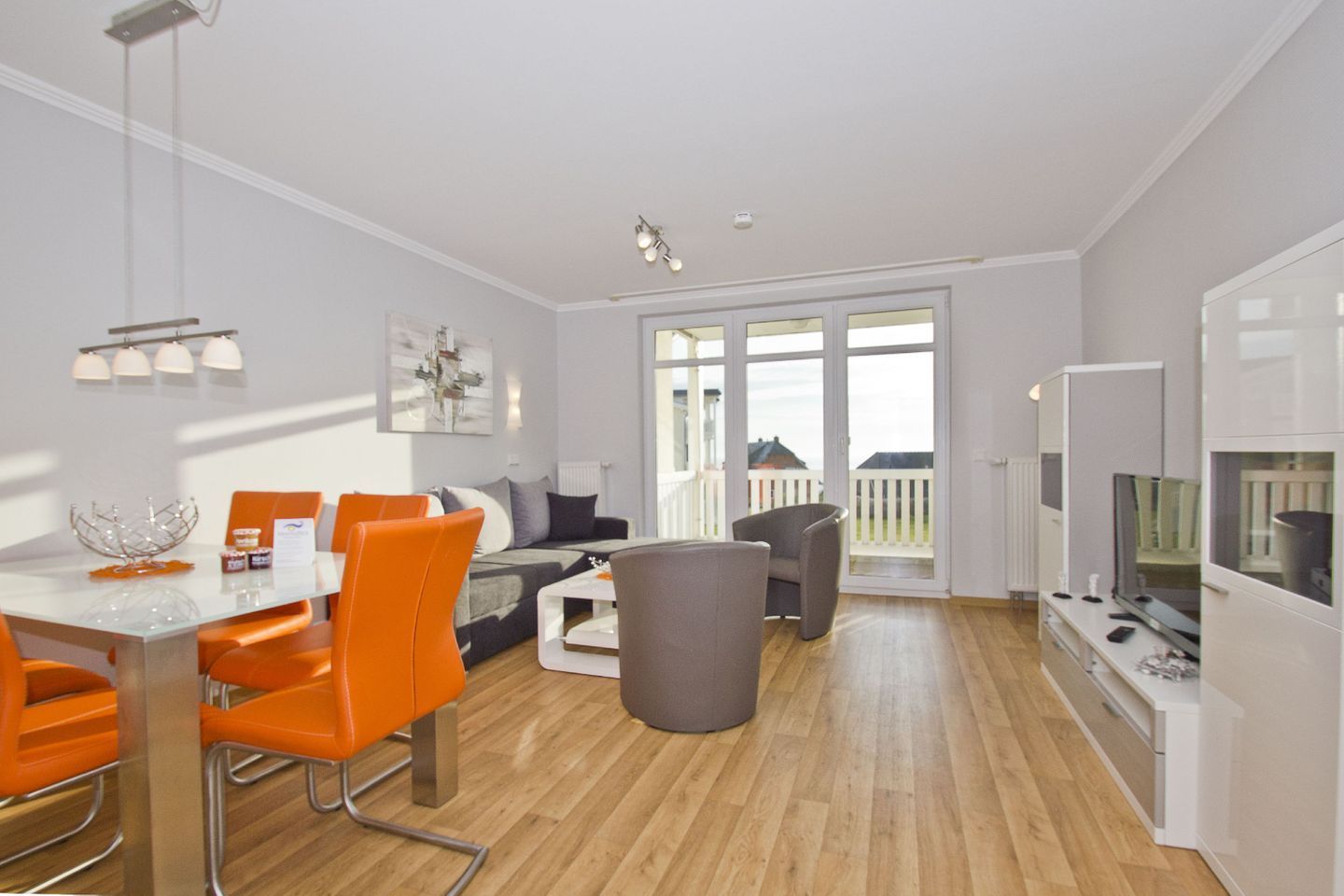 A modern living room with a dining area, a grey sofa, orange chairs, and a large window with a view.