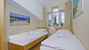 Une chambre avec deux lits simples, une fenêtre avec des rideaux, un tableau au mur et une petite table avec une lampe.