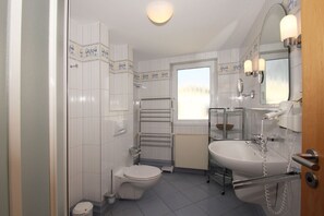 A compact bathroom with a toilet, a glass shelf, a sink with a mirror, and a hairdryer. - With sea view and balcony, use of swimming pool and sauna - sea view apartment 27 - (Göhren)