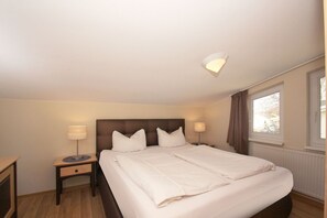 A hotel room with a large bed, two bedside tables, a nightstand, a window with curtains, and a ceiling light fixture. - With a view of the sea and a balcony, access to the pool and sauna - Sea View Apartment 27 - (Göhren)