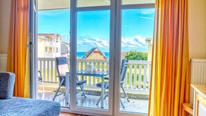A room with a sliding glass door leading to a balcony with a view of a house and the sea.