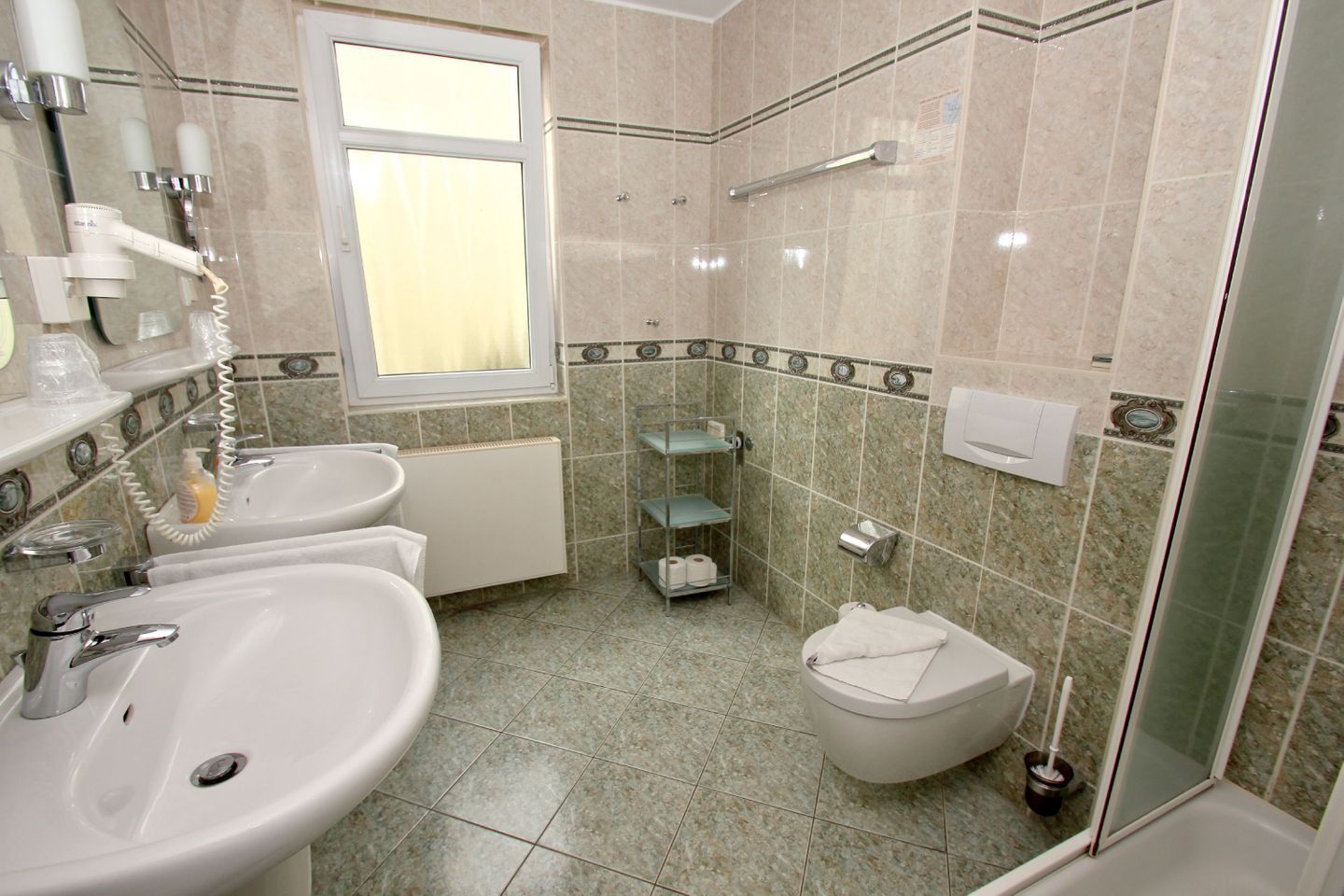 Ein Badezimmer mit zwei Waschbecken, einer Toilette, einer Dusche und einer Duschkabine aus Glas.