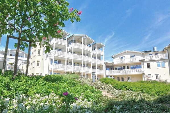 Ein mehrstöckiges Hotel mit Balkonen, umgeben von Grünpflanzen und weißen Blüten.
