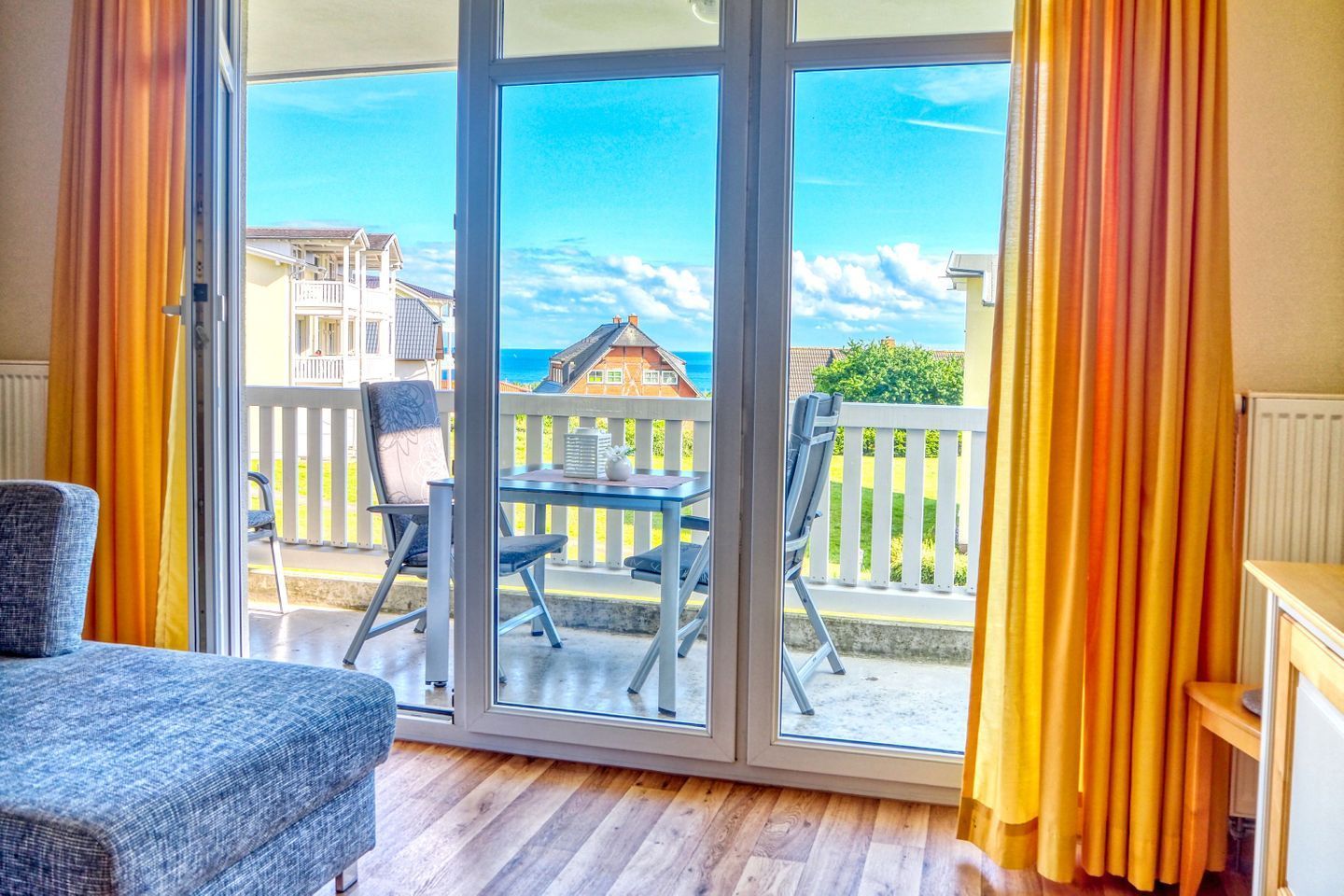 A room with a sliding glass door leading to a balcony with a view of a house and the sea.