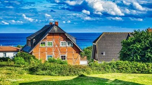 A traditional half-timbered house with a sloped roof, a visible chimney, and a view of the sea.