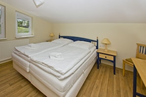 A double bed with white linens, a wooden nightstand with a lamp, a wooden chair, and a window with blinds. - With a view of the sea and a balcony; access to the pool and sauna - Sea View Apartment 18 - (Göhren)
