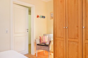A room with a wicker chair, a wooden wardrobe, and a door leading to another room. - With a view of the sea and a balcony; access to the pool and sauna - Sea View Apartment 21 - (Göhren)