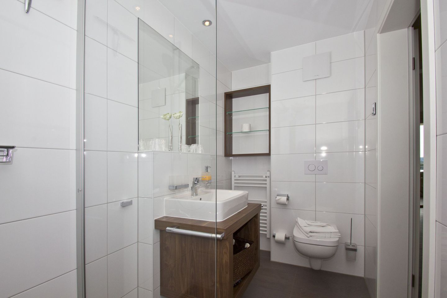 A modern bathroom with a glass shower enclosure, a wooden vanity, a white sink, and a toilet.