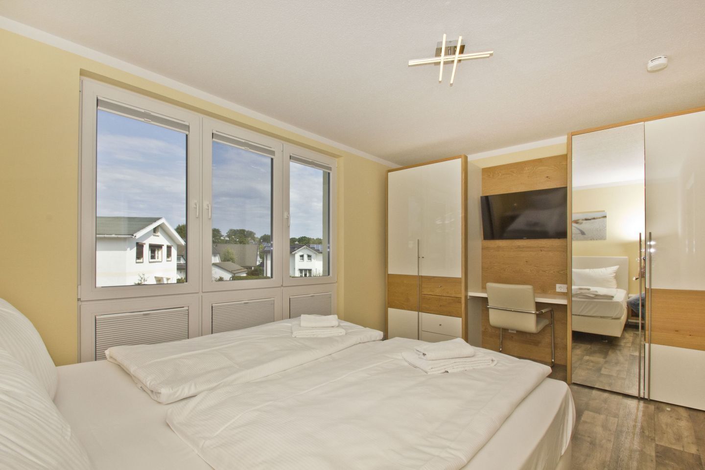 A modern bedroom with a large bed, a desk, and a wardrobe.