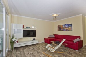 Un salon moderne avec un canapé rouge, un téléviseur à écran plat, un meuble blanc et un fauteuil à bascule.