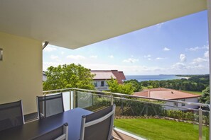 Un balcon avec une table et des chaises, donnant sur une maison avec un toit recouvert de tuiles rouges et offrant une vue sur la mer.