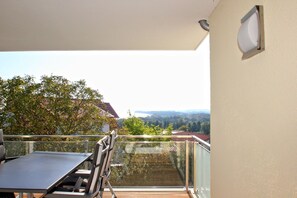A balcony with a table and chairs, overlooking a scenic view of trees and distant buildings. - With sea view and balcony, use of swimming pool and sauna - sea view apartment 64 - (Göhren)