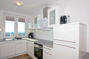 A modern kitchen with white cabinets, a built-in oven, and a coffee maker on the countertop. - With a view of the sea and a balcony, access to the pool and sauna - Sea View Apartment 64 - (Göhren)