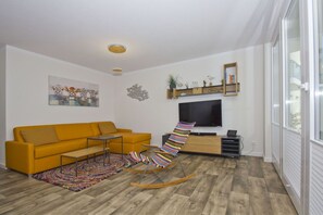 A modern living room with a yellow sofa, a colorful rocking chair, a flat-screen TV, and a wooden floor. - With a view of the sea and a terrace, access to the pool and sauna - Sea View Apartment 68 - (Göhren)