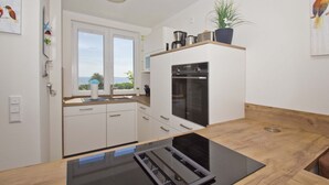 A modern kitchen with white cabinets, a built-in oven, and a window with a view. - With sea view and terrace, use of swimming pool and sauna - sea view apartment 68 - (Göhren)