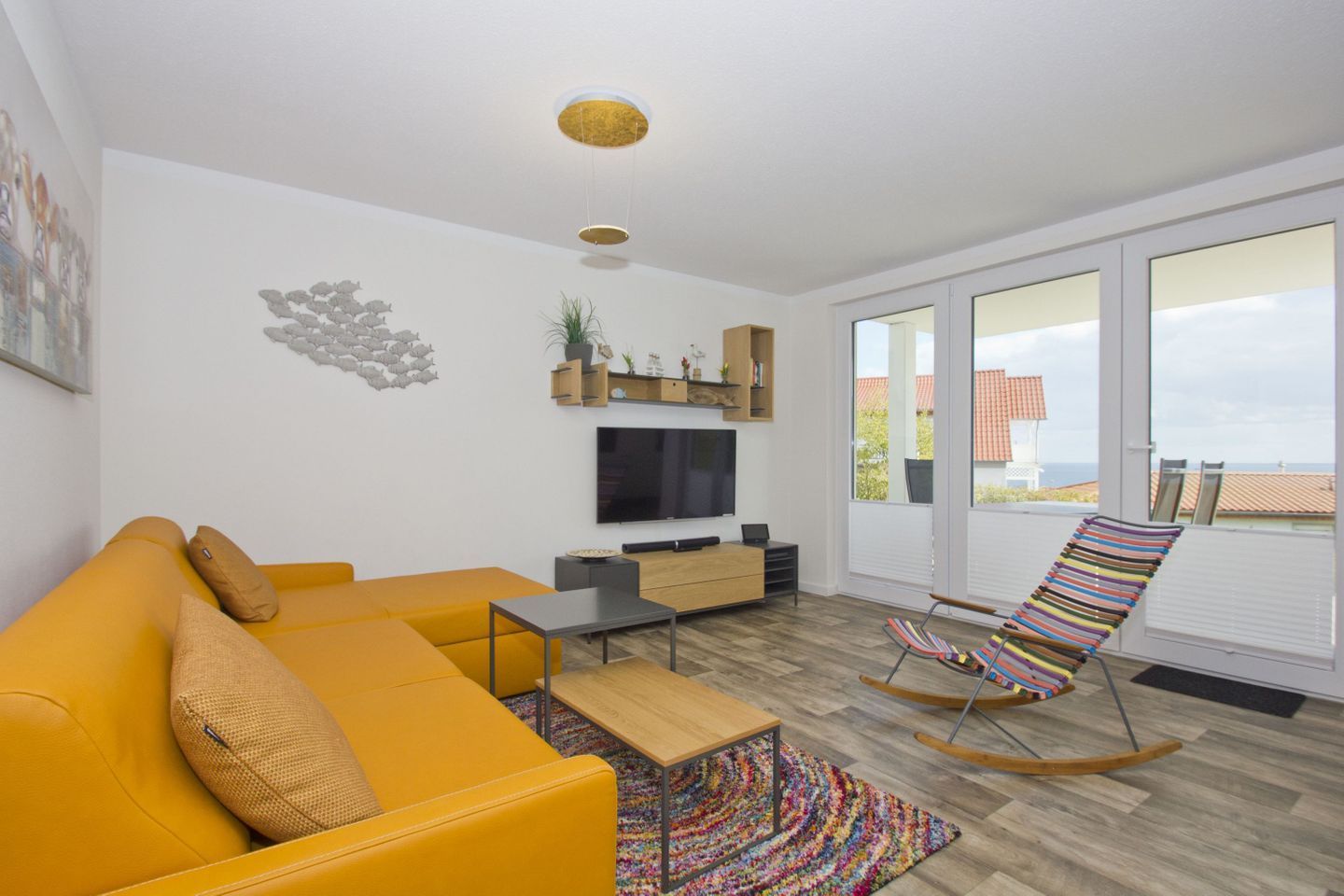 A modern living room with a yellow sofa, a TV, a wooden coffee table, and a colorful rocking chair.