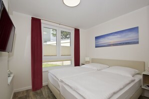 Habitación de hotel con cama, ventana con cortinas, un cuadro en la pared y televisor montado en la pared.