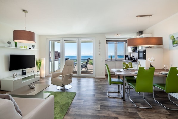 A modern living room with a flat-screen TV, a comfortable sofa, and a green rug. - With sea view and balcony, use of swimming pool and sauna - sea view apartment 70 - (Göhren)