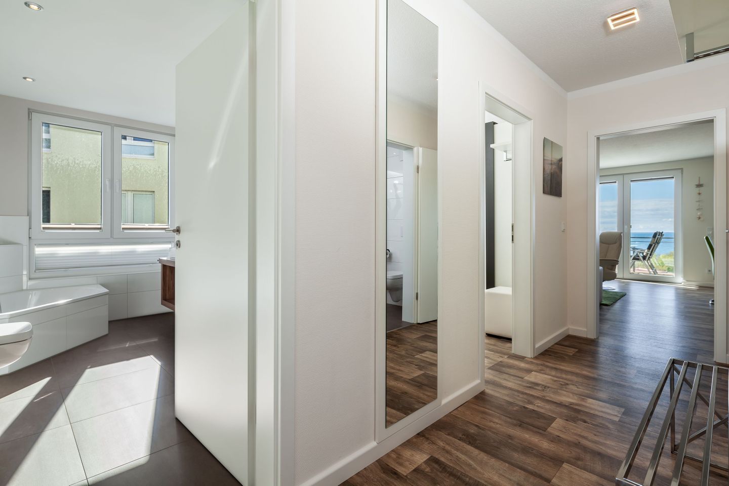 A modern bathroom with a bathtub, toilet, and shower. There is a large window providing natural light and a view of the outdoors.