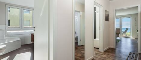 A modern bathroom with a bathtub, toilet, and shower. There is a large window providing natural light and a view of the outdoors.