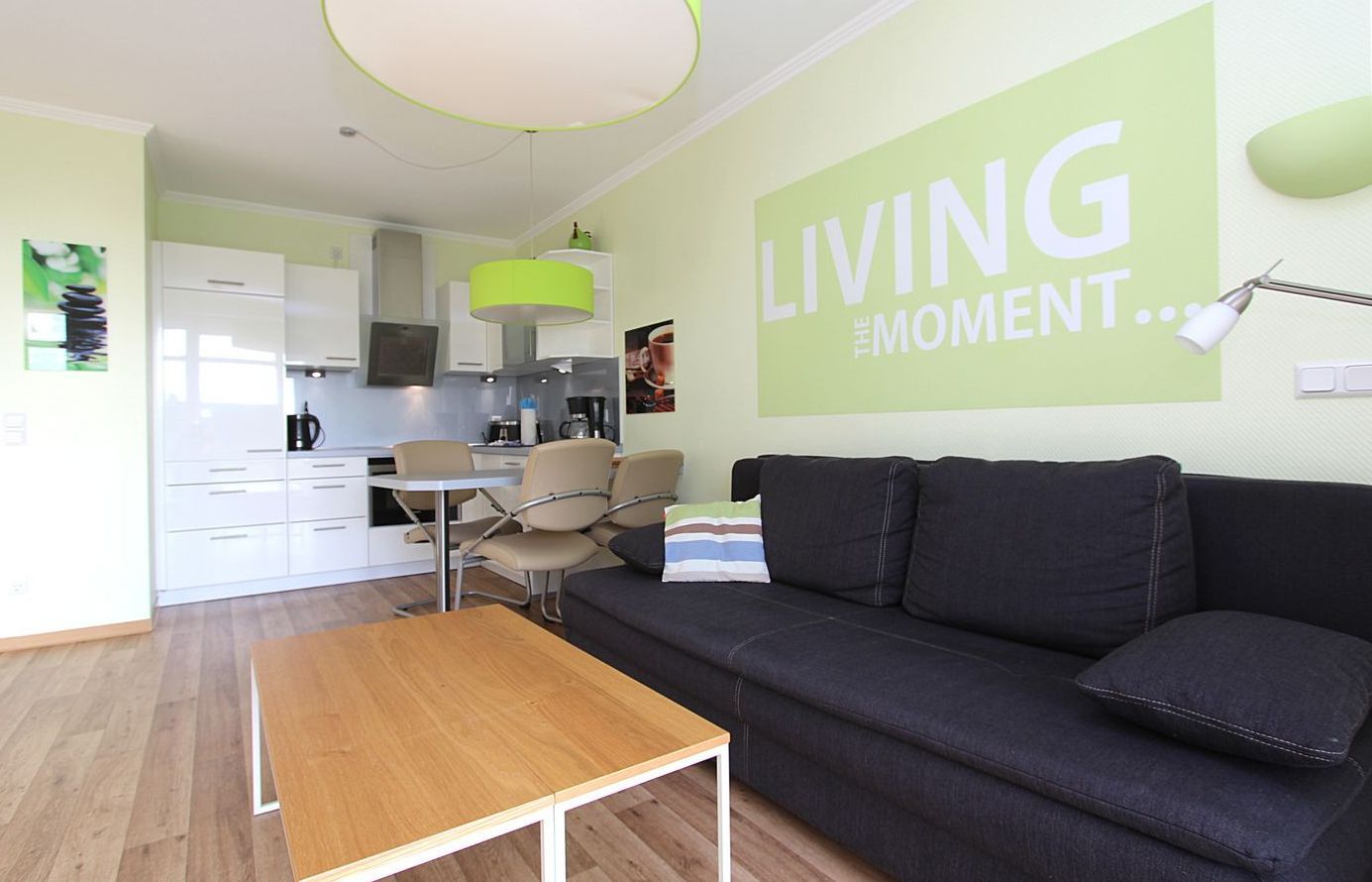A modern living room with a sofa, a wooden table, and a kitchen in the background.