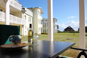 Et bord med en hvidvinflaske og et glas, foran udsigt til et boligkompleks.