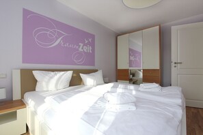A neatly made bed with white linens and pillows, a large mirror, and a wall with a purple sign.