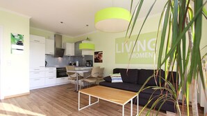 A modern living space with a kitchen, dining area, and a sofa. - Terrace, free use of the AHOI adventure pool and sauna - Sea view apartment 31 - (Göhren)