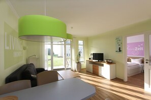 A modern living room with a dining area, a TV, and a bedroom with a bed and a bathroom visible through an open door.