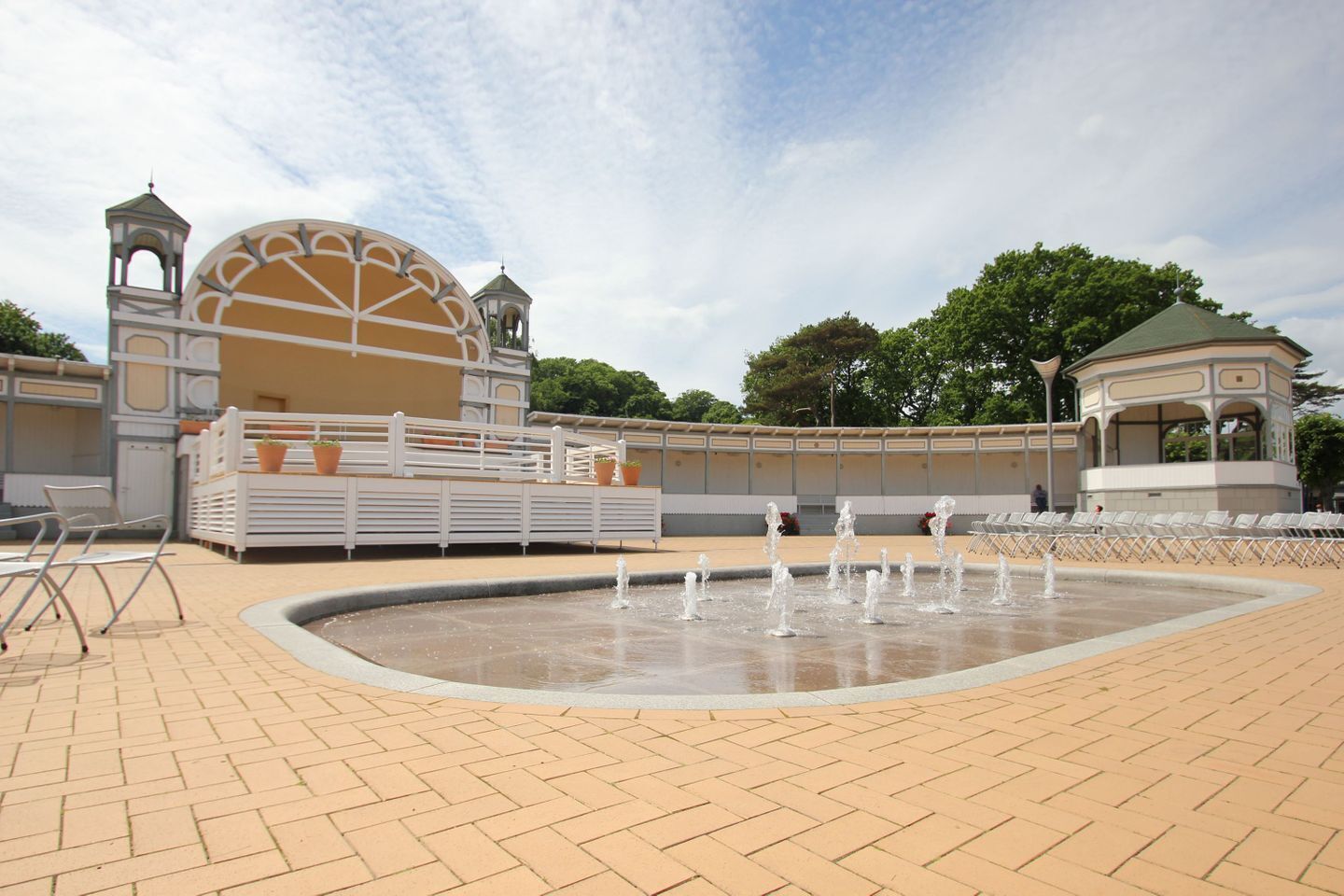 Una plaza pública con una fuente, zonas de estar y un edificio con una cúpula y torres.