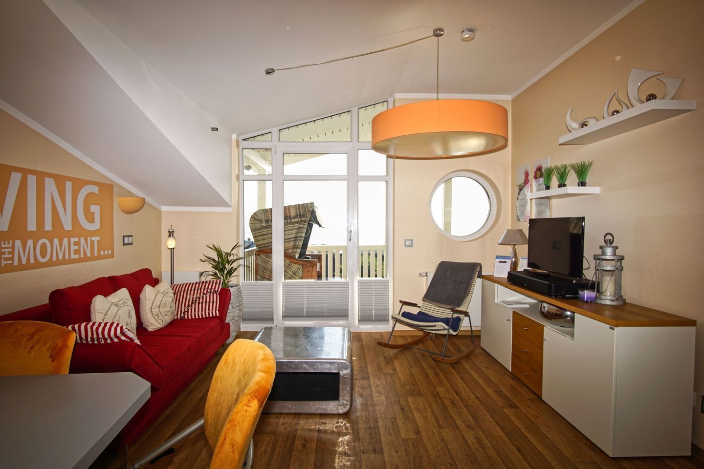A modern living room with a red sofa, a wooden dining table, and a kitchen area with a TV and a small fridge.
