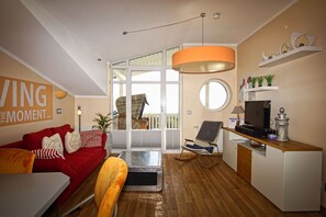 A modern living room with a red sofa, a wooden dining table, and a kitchen area with a TV and a small fridge.