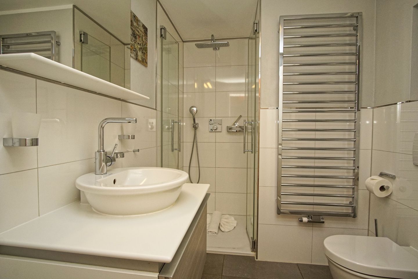 A modern bathroom with a white sink, a glass shower enclosure, and a towel rack.