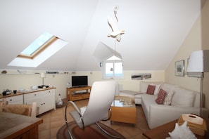 Ein geräumiges Loft-Apartment mit hoher Decke, Dachfenster und einer gemütlichen Wohnbereits mit Sofa, Sessel und Esstisch.