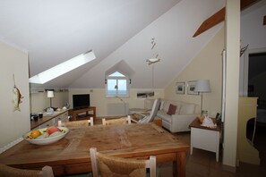 Een gezellig loft-appartement met een eethoek, een bank, een televisie en uitzicht op de lucht via een dakraam.