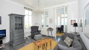 Una sala de estar moderna con un sofá gris, una mesa de centro de madera, un sillón gris, un mueble con puertas de vidrio y un ventanal grande.