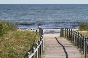 A wooden boardwalk leading to a beach with a person in the distance.