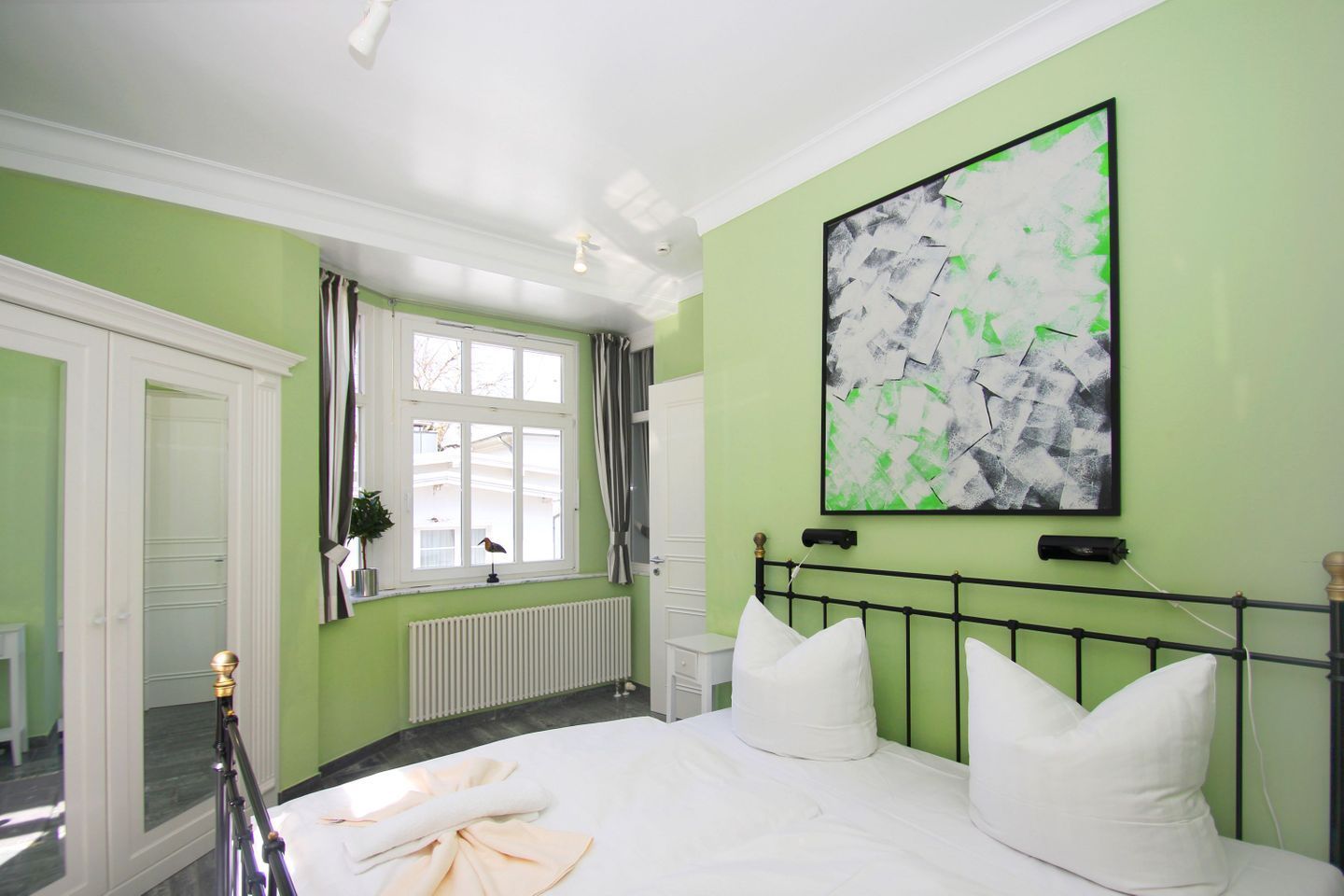 A bedroom with a bed, a window, a radiator, and a painting on the wall.