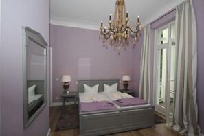 Une chambre à coucher avec un lit, deux tables de chevet, un lustre et une fenêtre avec des rideaux.