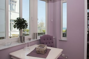 A room with a view of the sea, a window with a potted plant, a cushioned chair, and a table with a glass and a basket. - Die Ausstattung der Ferienwohnung Nr. 02 in der Villa Strandeck - Villa Strandeck (Binz)