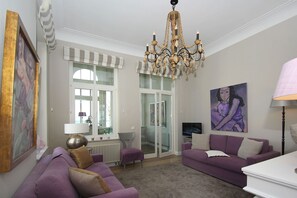 Ein Wohnzimmer mit einer Chandelierleuchtre, violetten Sofas, einem Fernseher und Kunstwerken an den Wänden.