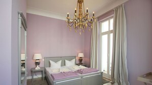 Une chambre à coucher avec un lit double, deux tables de chevet avec des lampes, un lustre, une grande fenêtre avec des rideaux et un miroir sur le mur.