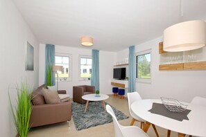 A modern living room with a sofa, a round coffee table, and a dining area with a table and chairs. - Beachfront vacation rental with a terrace, access to the pool and sauna - Rex Rugia - Rex (Göhren)