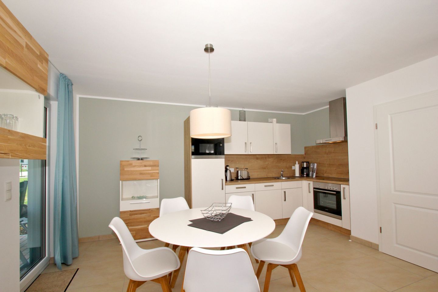 Une cuisine moderne avec des meubles blancs, un plan de travail en bois et un coin repas comprenant une table et des chaises blanches.